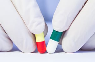 gloved fingers holding 2 pill capsules